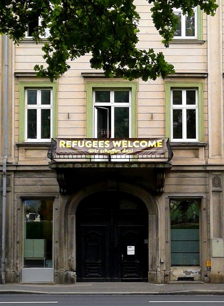 Ein Banner mit der Aufschrift "Refugees Welcome! Wir schaffen das!" hängt auf einem Balkon eines alten Hauses